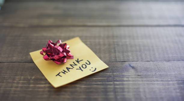 A handwritten thank you note with a red bow on a wooden surface