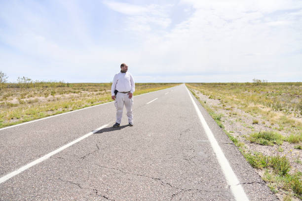 istock Man standing in the middle of a quiet empty road looking to the side 2170571675