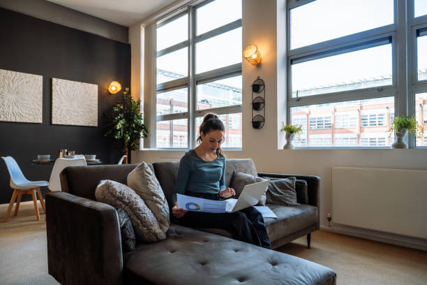 istock White woman working from home sitting on a cozy sofa with a laptop and documents in a modern living room setting. 2170575489
