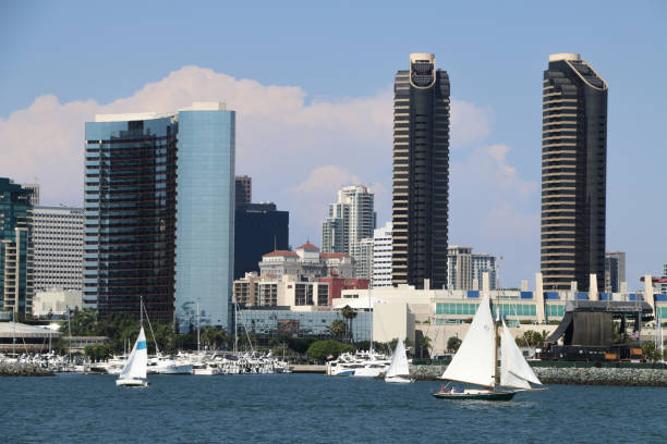 San Diego Bay, San Diego, CA, USA - October 1, 2014. Sailboats tack over the  waters of San Diego Bay, the city’s iconic skyline serves as a dramatic backdrop. The wind blows hard against their sails as they cut across the bay. Downtown San Diego’s towering skyscrapers rise majestically in the distance, and stand as a testament to San Diego's blend of natural beauty and urban sophistication. Also in view are the San Diego Convention Center, sailboats and other recreation boats docked in the marina, and to the right is a concert stage where bands often play. The scene is a perfect harmony of serene seascape and vibrant city life, capturing the essence of San Diego’s unique charm.