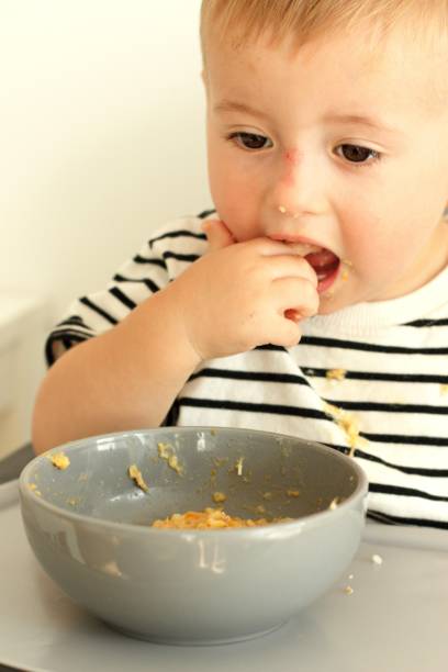 istock Little serious child eats independently with a spoon while sitting on a high chair 2170580416