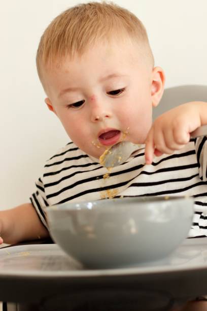 istock Little serious child eats independently with a spoon while sitting on a high chair 2170580427
