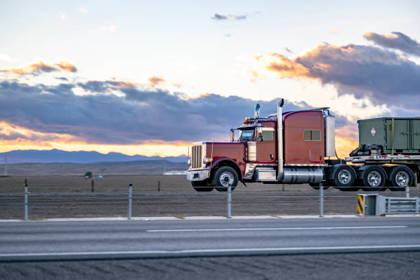 istock Dark red classic big rig semi truck with extended cab transporting fastened cargo on flat bed semi trailer running on the flan highway road at sunset time 2170582186