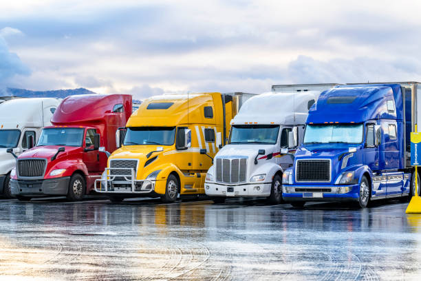 Different color and makes big rig semi trucks with semi trailers standing in row on the truck stop parking lot early morning with wet after rain surface stock photo