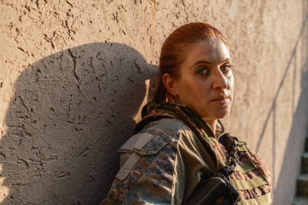 Military training: armed female  soldier in camouflage gear taking a break armed with with rifle against the outdoor wall, during practising military discipline and teamwork.