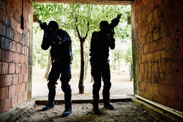 Military training: two soldiers in black camouflage gear tactical move with rifles inside  abandoned brick building, practising military discipline and teamwork during a close-quarters operation.