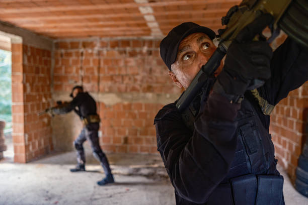 Military training: two soldiers in black camouflage gear tactical move with rifles inside abandoned brick building, practising military discipline and teamwork during a close-quarters operation.