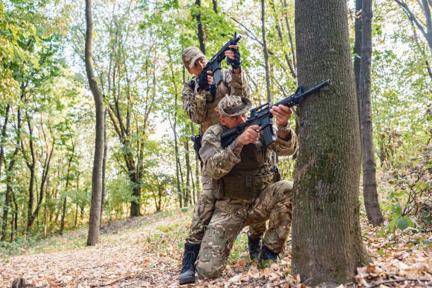 Military training: two soldiers- male and female, in camouflage gear tactical move with rifles in wooded area during military training, practising military discipline and teamwork during outdoor operation.