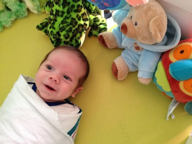 A baby boy lies happily on his play mat wrapped in a blanket.