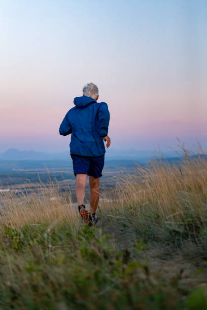 Senior man runs through grasses at sunset