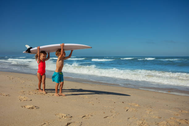 istock Kids walking with surfboard on shoulders at sunny ocean beach 2170591517
