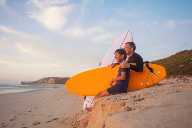 istock Man and young boy with surfboards at the seashore during dusk 2170591575
