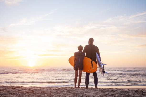 istock Two surfers hugging stand on sand watching the sunset over ocean 2170591632