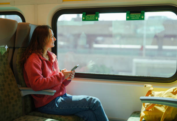 Woman using smartphone and looking through the window traveling by train in Canada