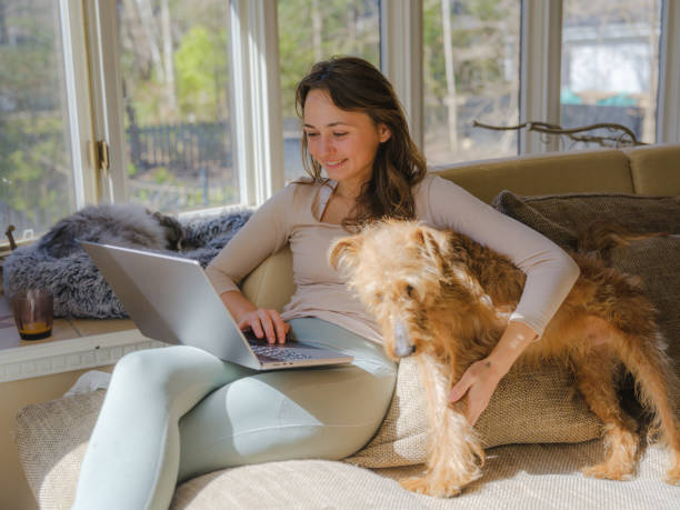 istock Woman cuddling with dog on the sofa using laptop on sunny afternoon 2170593482