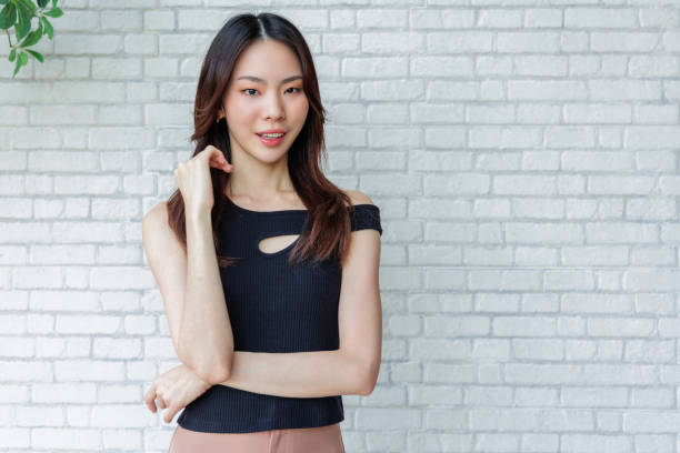 istock Smiling Young Woman Posing Casually in Black Top Against White Brick Wall 2170595234