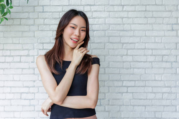 istock Smiling Young Woman Posing Casually in Black Top Against White Brick Wall 2170595237