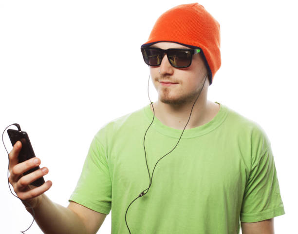 technology and people concept - young man wearing green t-shirt  listening music and using smartphone, isolated on white