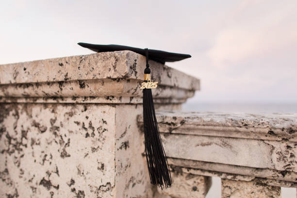 istock A Black Graduation Cap with a Black 2025 Tassel Lying on a Stone Wall Overlooking the Palm Beach, Florida Seashore 2170604234