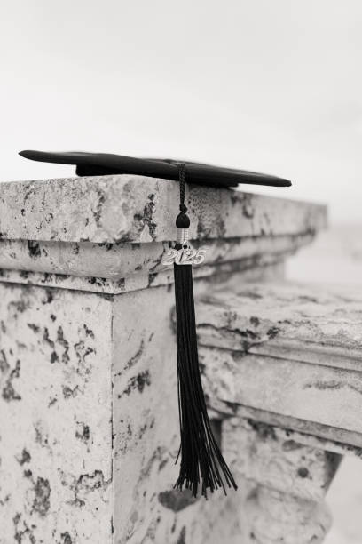 istock A Black Graduation Cap with a Black 2025 Tassel Lying on a Stone Wall Overlooking the Palm Beach, Florida Seashore 2170604246