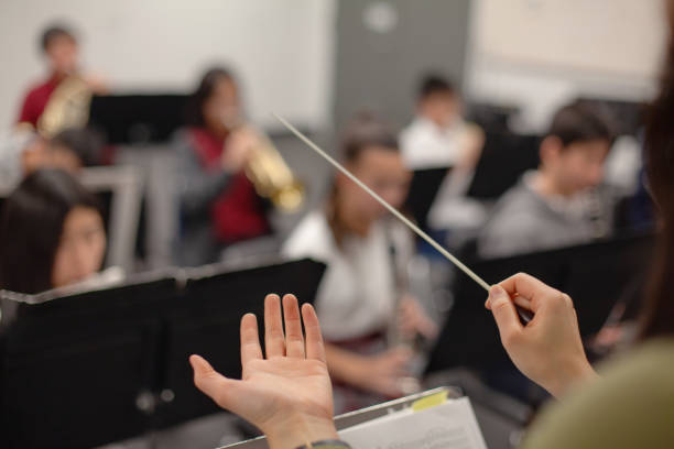 blick auf die band, den lehrer, den lehrer, den dirigentenhände, die das orchester der musikaufführung im orchester der mittelstufe leiten, die im klassenzimmer üben, zusammen in einer gruppe von menschen - dirigent stock-fotos und bilder