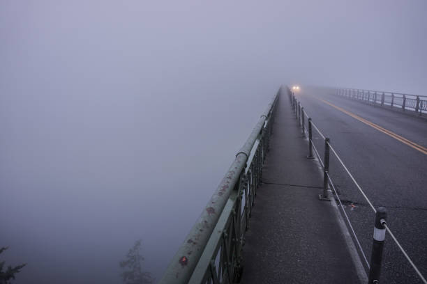 headlights of car shine through the fog on bridge at Deception Pass in the morning