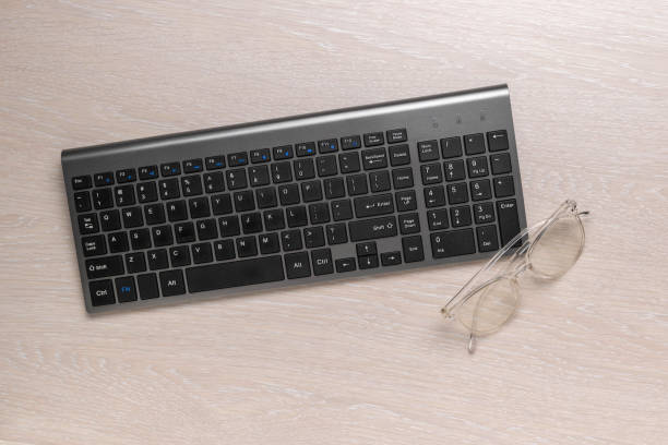 istock Wireless Keyboard and Glasses on Wooden Desk - Modern Office Workspace 2170621627