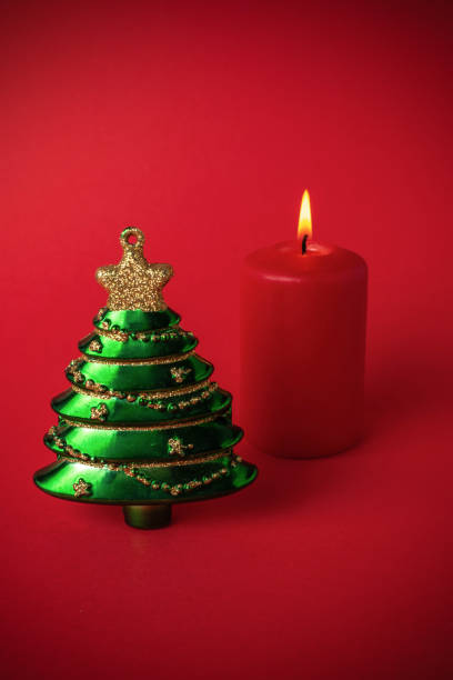 Green Christmas Tree Ornament and Red Candle on Red Background