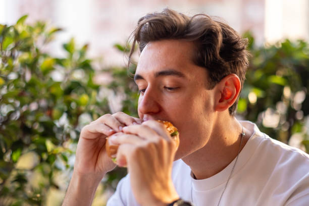 istock Handsome young man eating fast food hamburger outside 2170630244