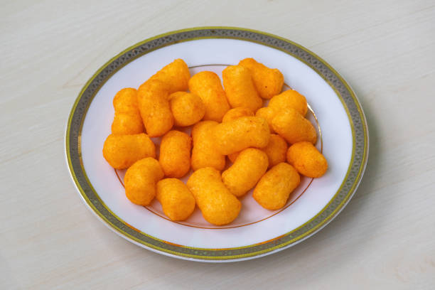 Cheese flavored snacks crackers chips on a white plate on light a wooden background.