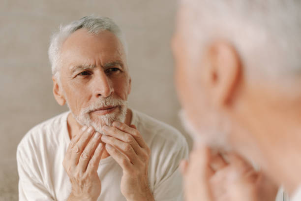 istock Senior man touching his beard looking at mirror in bathroom 2170643747