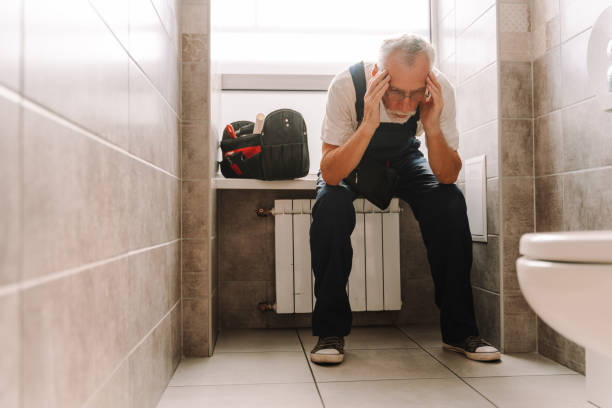 istock Senior plumber suffering headache sitting on radiator in bathroom 2170643867
