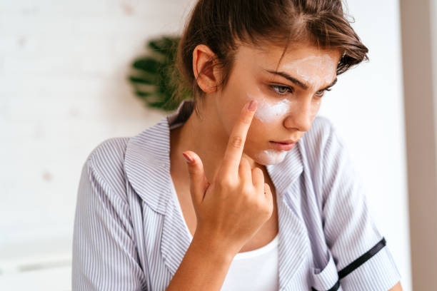 istock Young woman applying moisturizer cream on her face 2170656371