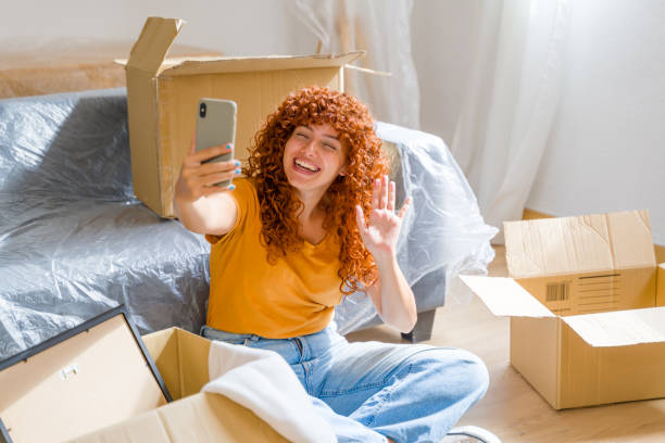 istock Happy woman having video call while sitting on floor among cardboard boxes 2170657157