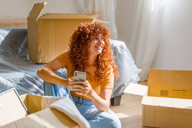 Woman using smartphone and relaxing on moving day