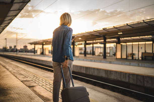 istock Mature woman wait for the train and hold cellphone and suitcase 2170657448