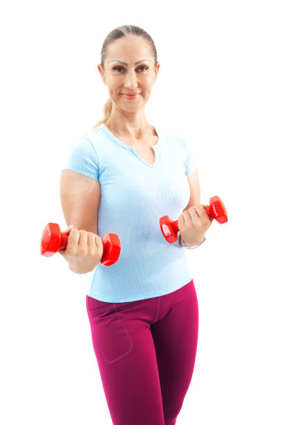 Smiling woman lifting red dumbbells while performing bicep curls, focusing on arm strength and fitness, isolated on a white background.
