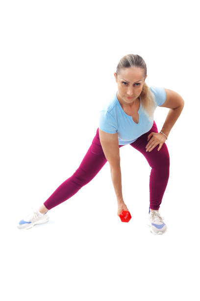 Focused woman doing a side lunge while holding a red dumbbell, targeting leg and arm muscles for strength and flexibility, isolated on a white background.
