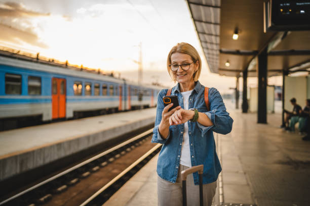 istock Mature woman wait for the train, use cellphone and walk with suitcase 2170659004