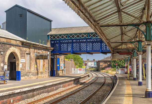 Bridlington, UK.  August 20, 2024.  Historic railway station platform with rails curving into the distance. Architectural columns support a canopy. A footbridge connects the platforms and an arched entrance is on one side.