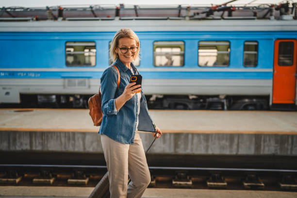 istock Mature woman wait for the train, use cellphone and walk with suitcase 2170659229