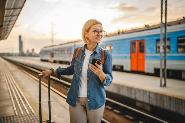 istock Mature woman wait for the train, use cellphone and walk with suitcase 2170659419