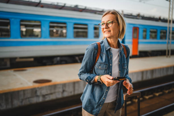 istock Mature woman wait for the train, use cellphone and walk with suitcase 2170659466