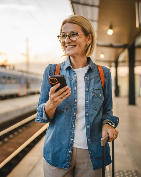 istock Mature woman wait for the train, use cellphone and walk with suitcase 2170659653