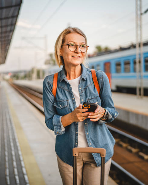 istock Mature woman wait for the train, use cellphone and walk with suitcase 2170659756