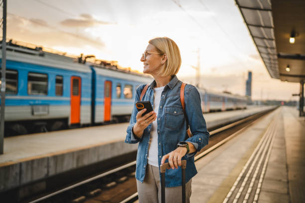 istock Mature woman wait for the train, use cellphone and walk with suitcase 2170659969