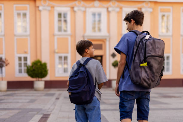 istock Back View of Two Brothers With a Backpack in Front of School Building 2170661127