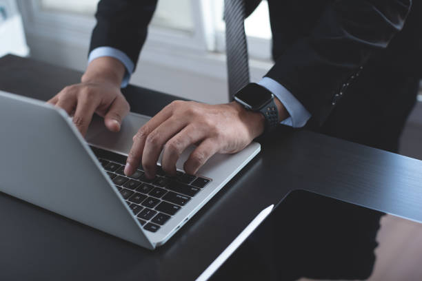 istock Businessman in black suit busy working on new project with notebook computer, digital tablet on table at office. Business man standing at desk, hands typing on notebook computer 2170670026