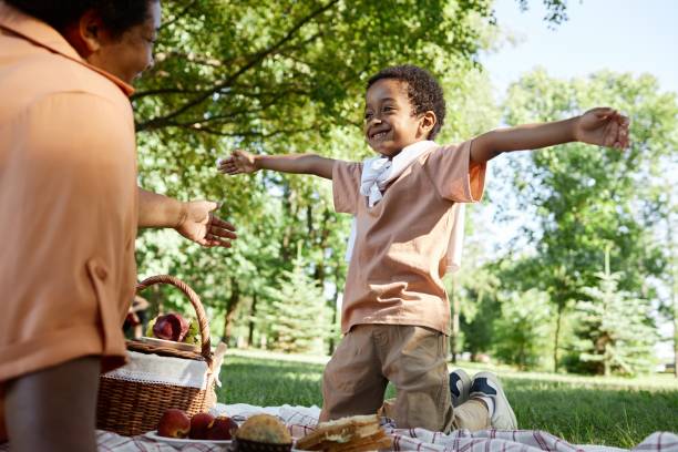 Low angle shot of African American boy ready to hug his beloved granny while they having picnic together in park