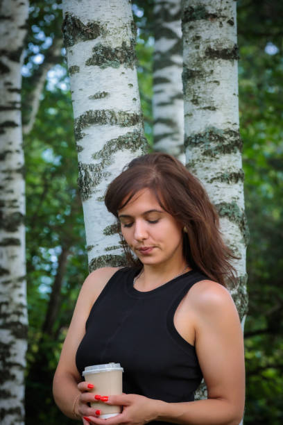 A serene Caucasian woman enjoys a moment beneath a willow, gentle sunlight filtering through the leaves around her.